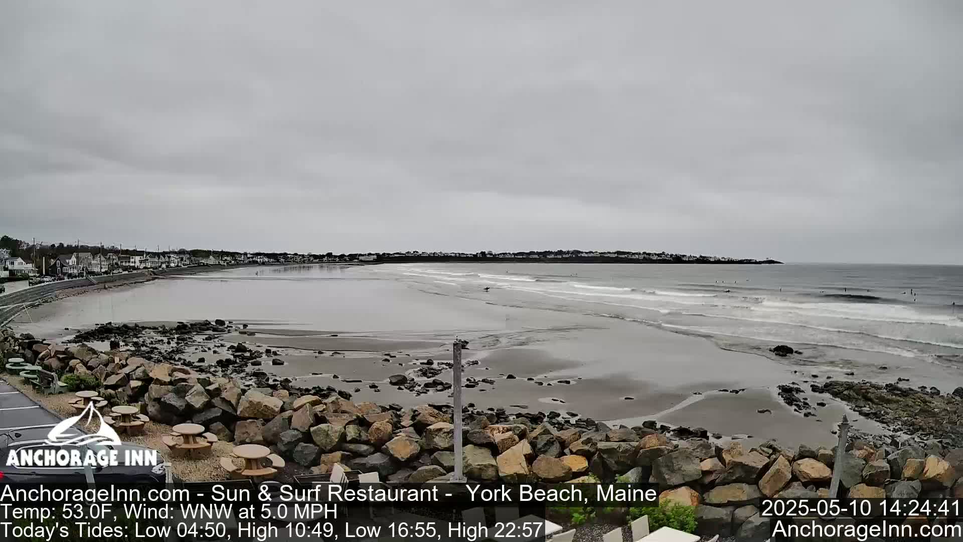 A rocky shoreline with a few people surfing in the ocean under an overcast sky.