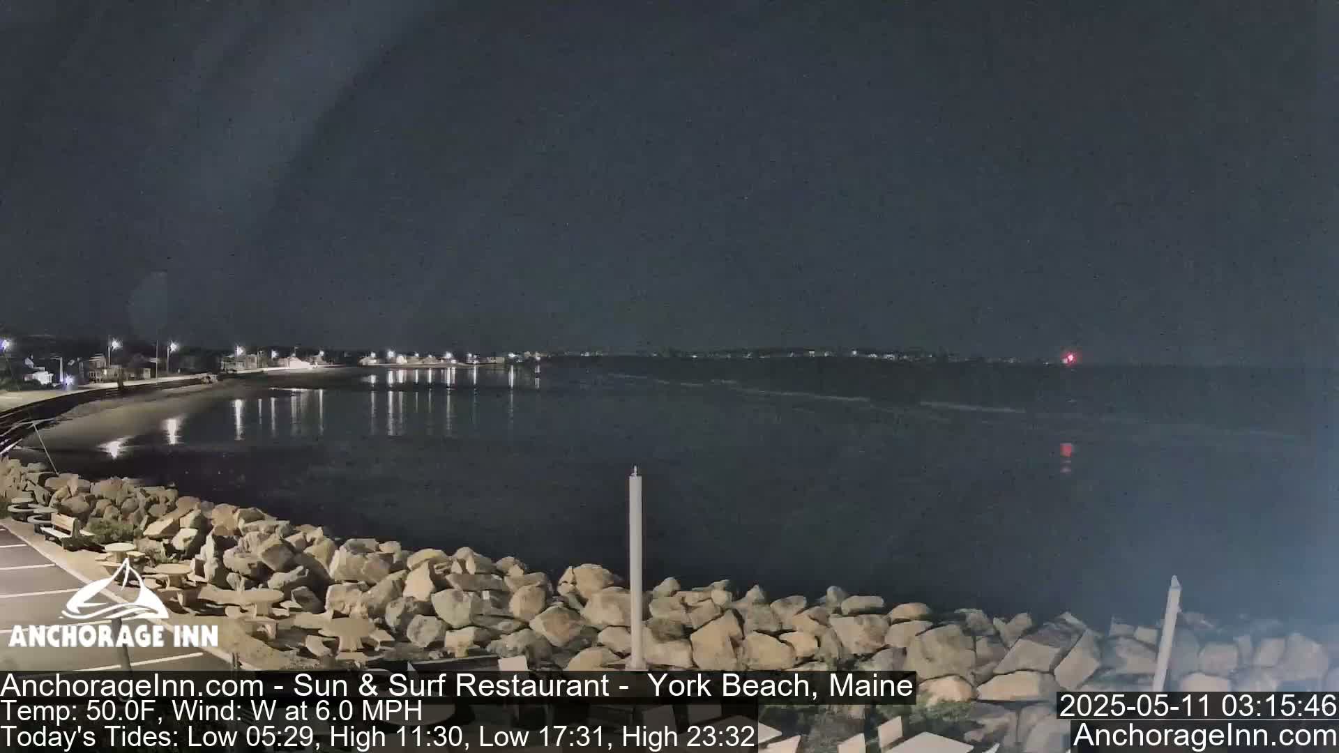 A nighttime view of a rocky shoreline and calm ocean under a dark sky.