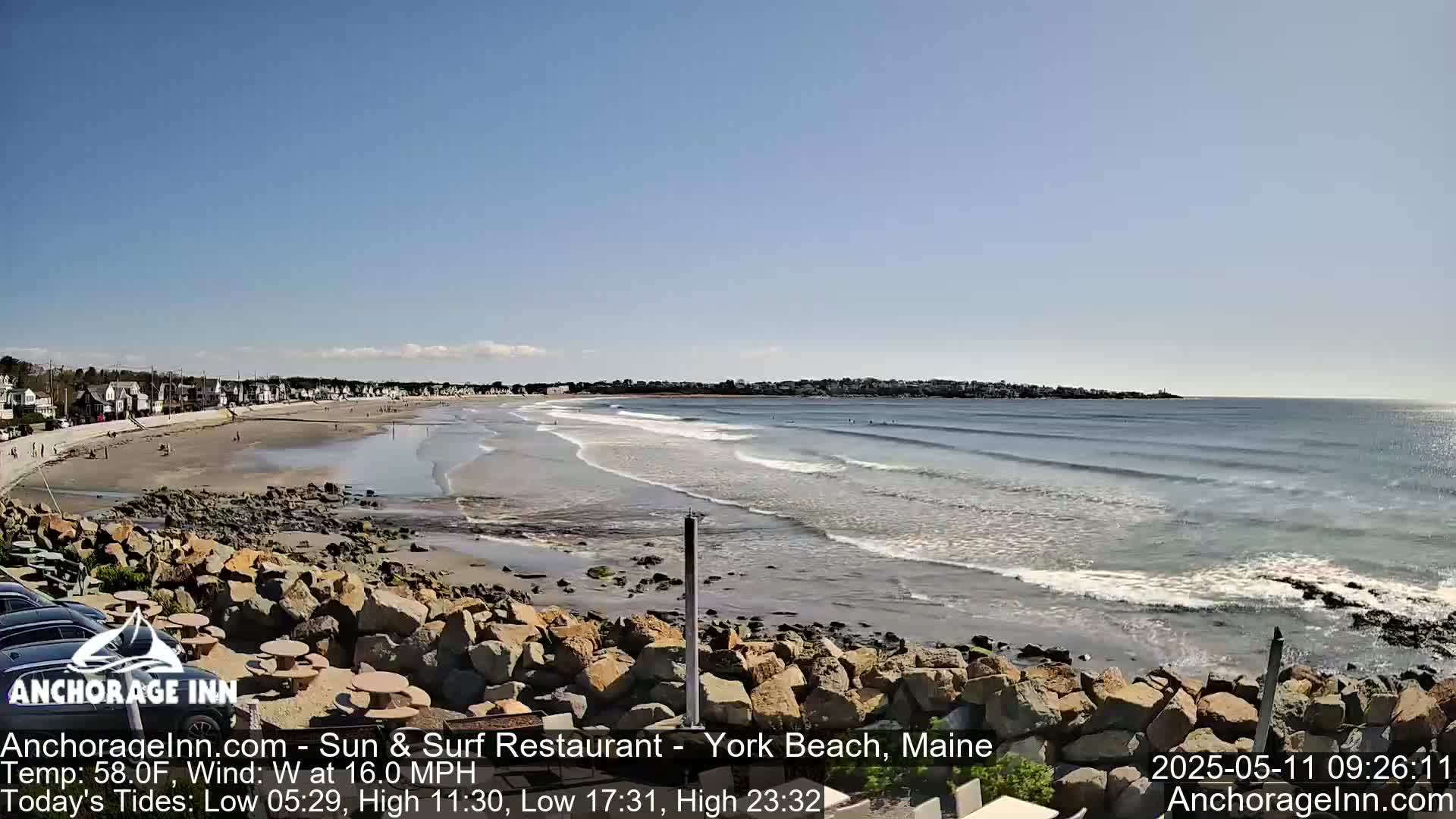 A sandy beach with gentle waves laps a rocky shoreline under a clear blue sky.