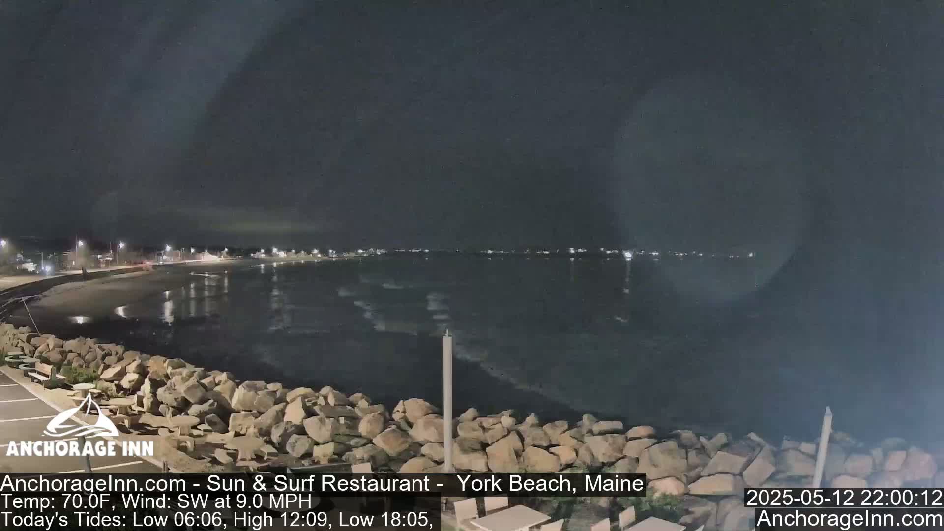 A nighttime view of a rocky shoreline and calm ocean under a dark sky.