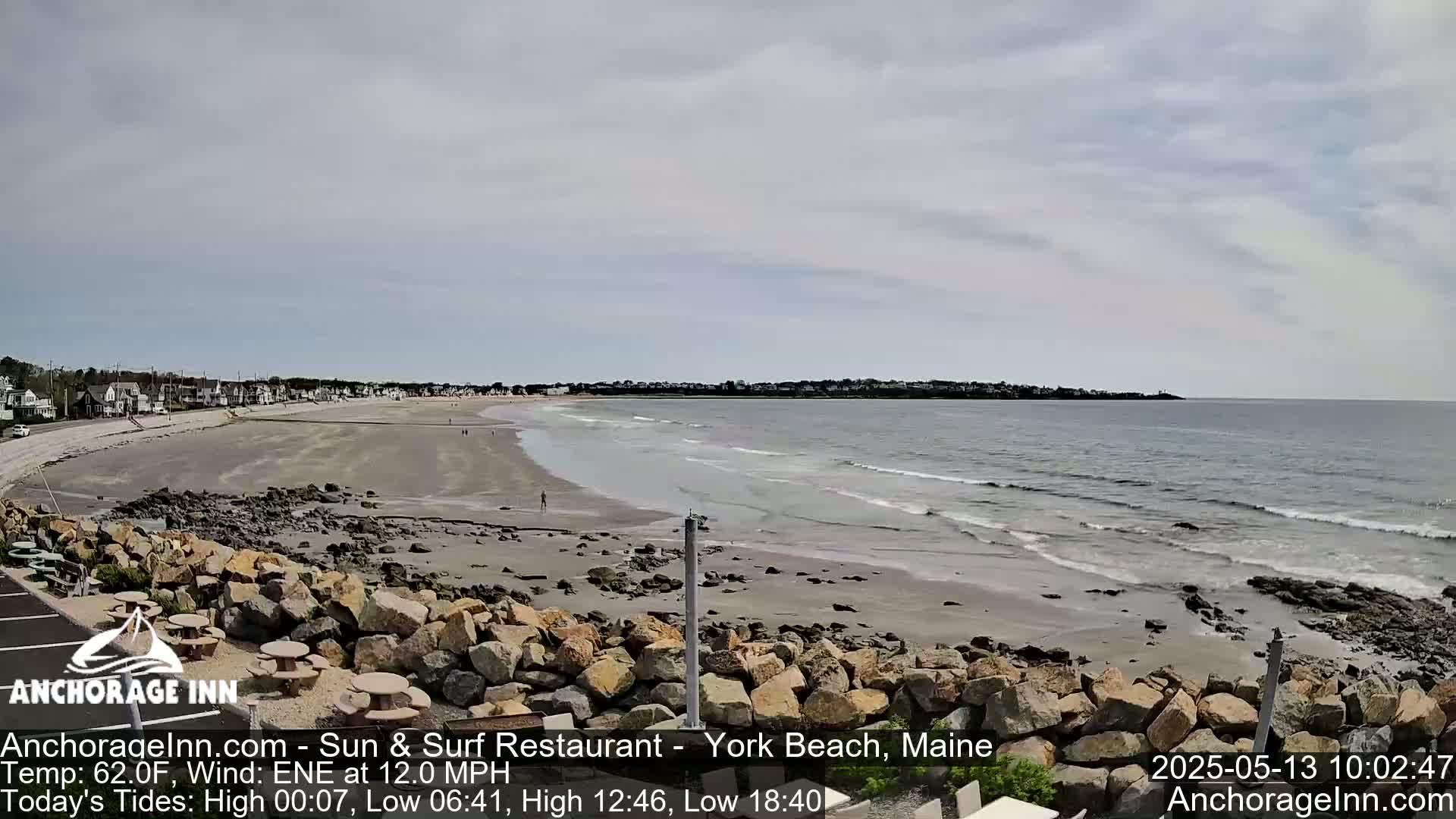 A sandy beach with gentle waves and a partly cloudy sky stretches toward a town in the distance.