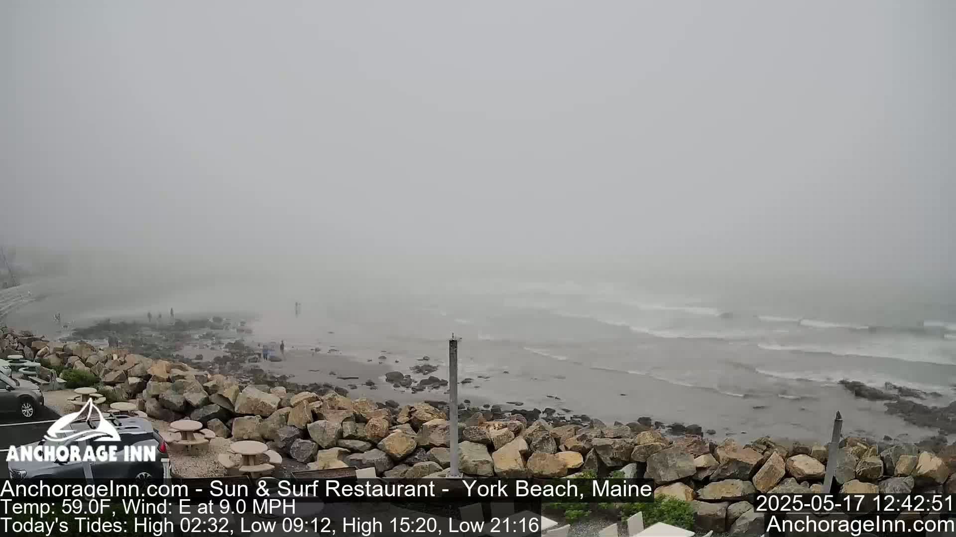 A foggy beach scene shows a rocky shoreline with small waves rolling in under a gray sky.