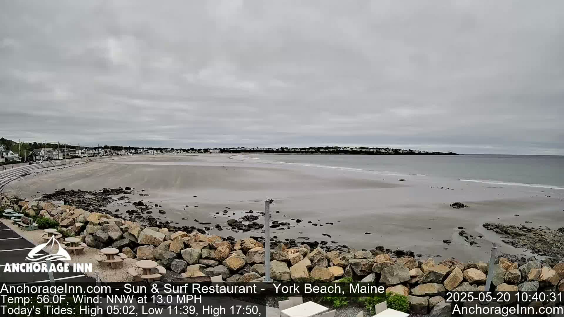 A wide sandy beach stretches towards a calm ocean under an overcast sky.