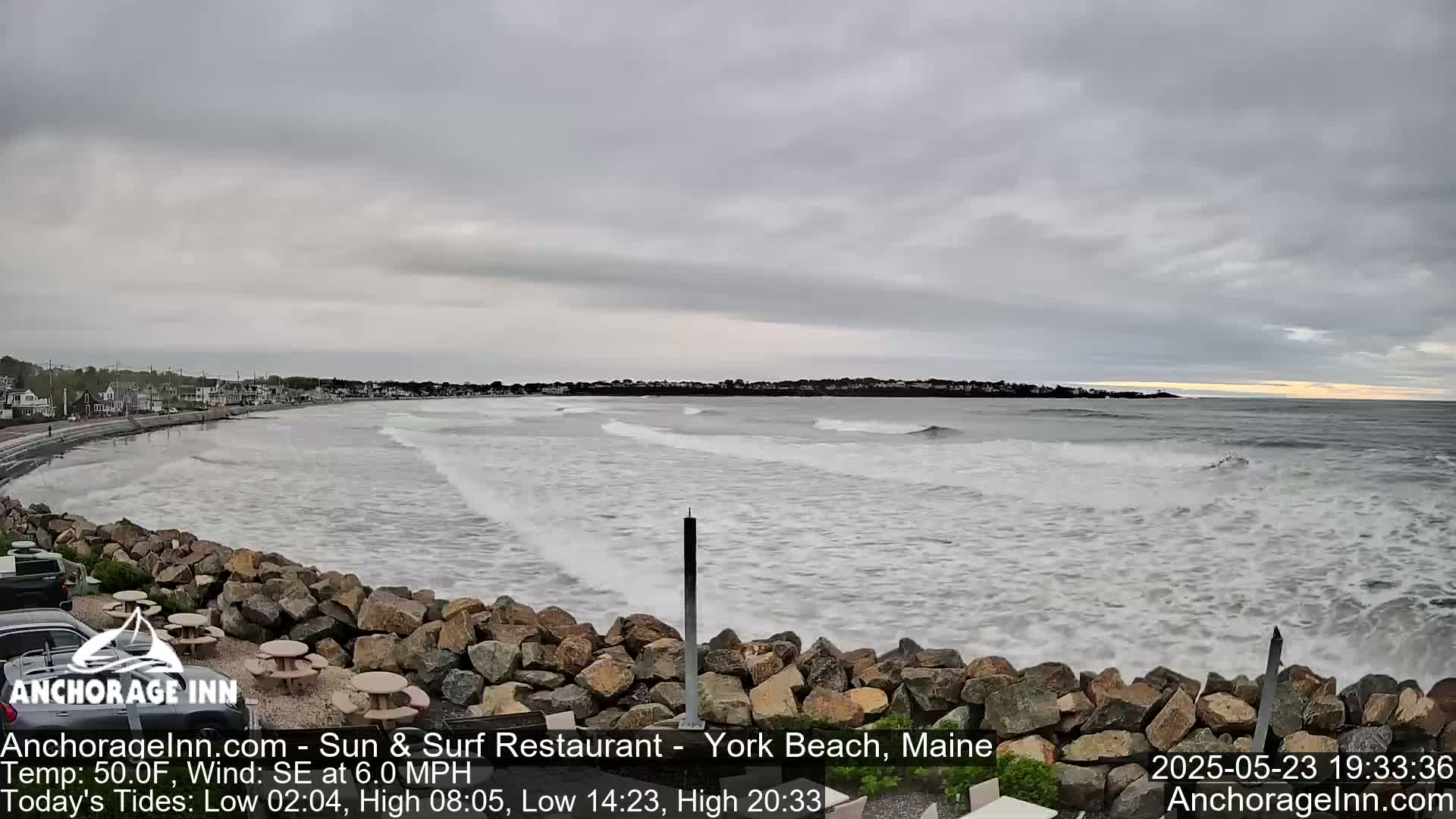 A rocky shoreline with a few picnic tables overlooks a choppy ocean under an overcast sky.