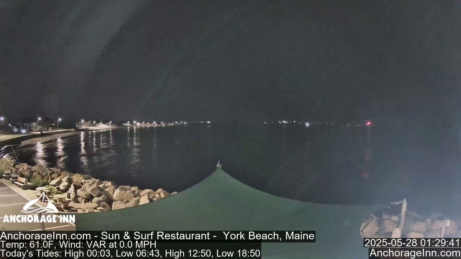 A nighttime view of a calm, dark body of water with a rocky shoreline and distant lights.
