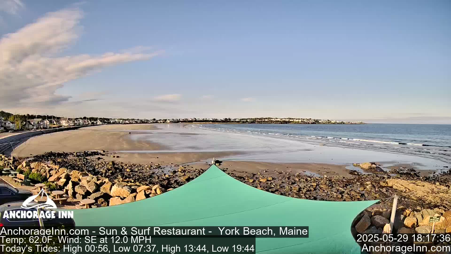 A sandy beach with a rocky shoreline and calm ocean waves under a partly cloudy sky.