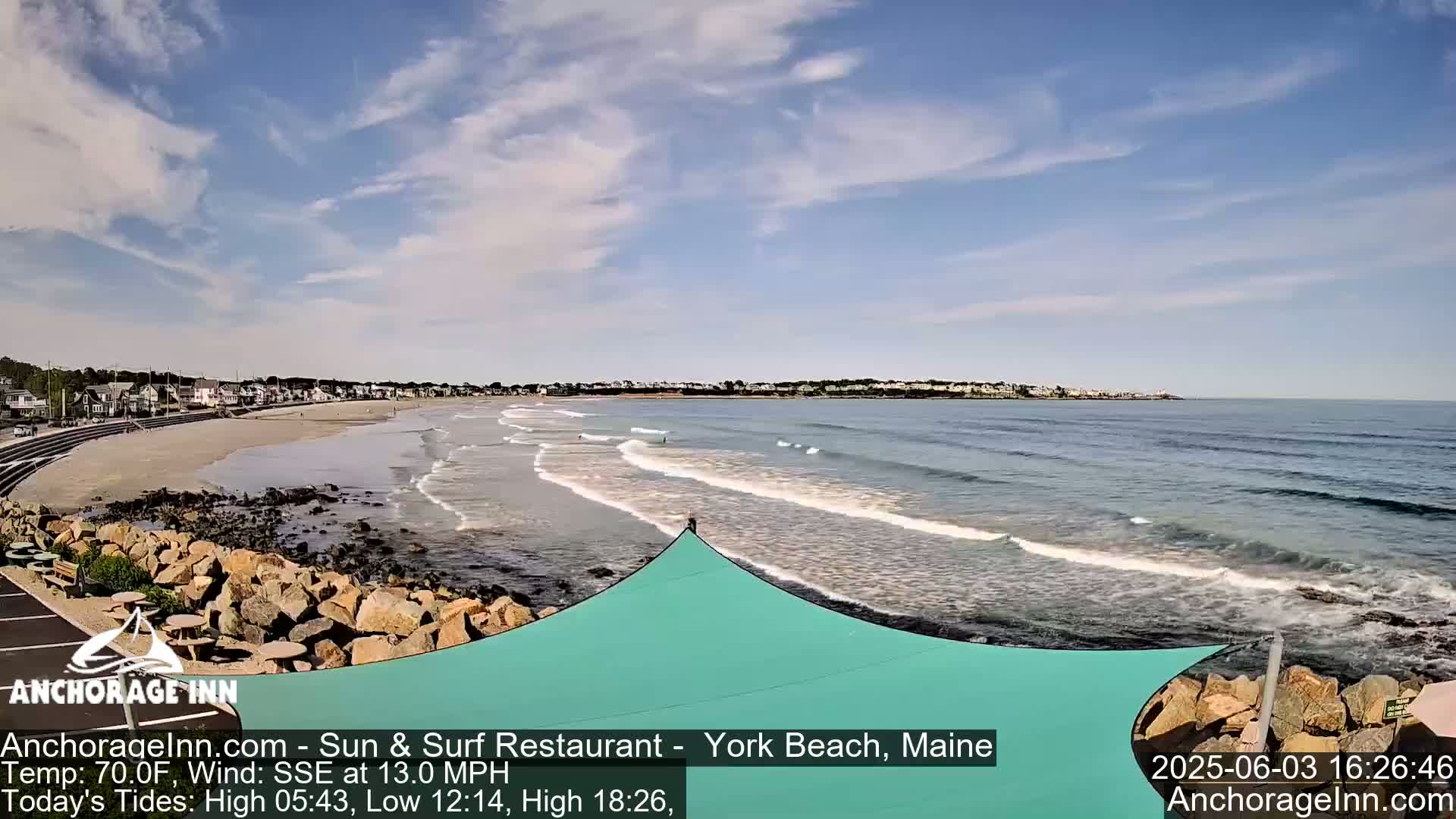 A partly cloudy beach scene shows a sandy shore with gentle waves lapping at the sand under a mostly clear sky.