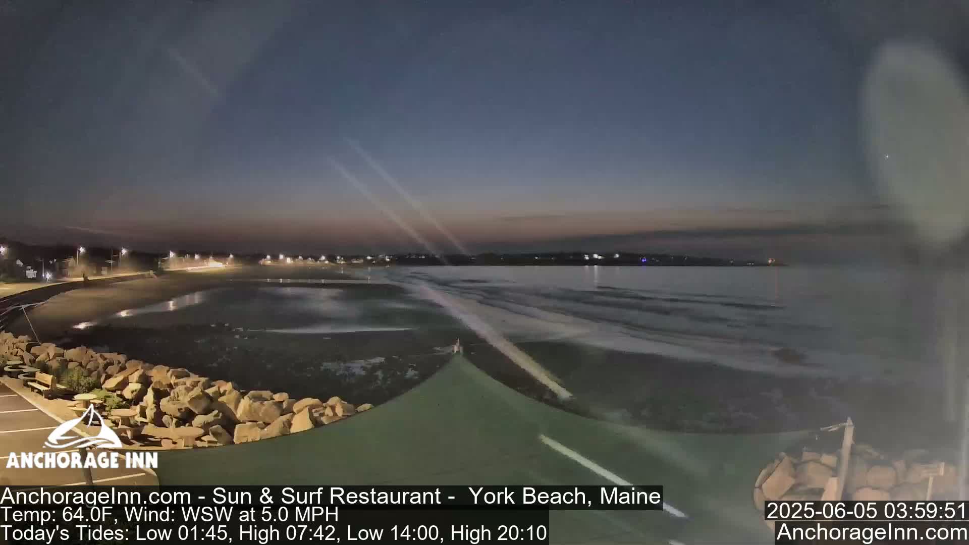 A dark, calm beach at twilight with gentle waves lapping the shore, under a mostly clear sky.