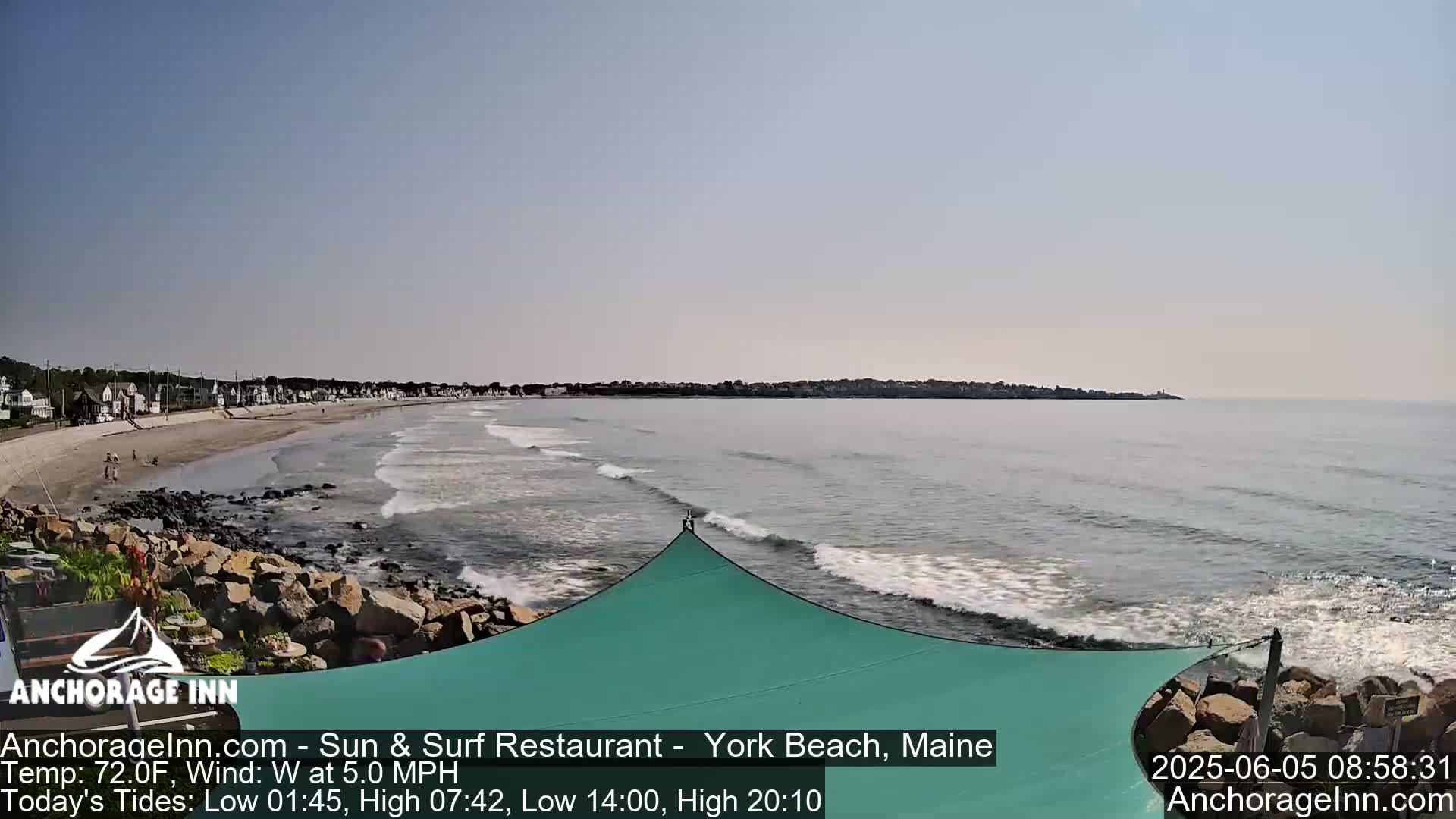 A sandy beach with gentle waves under a clear sky features a teal shade structure in the foreground.