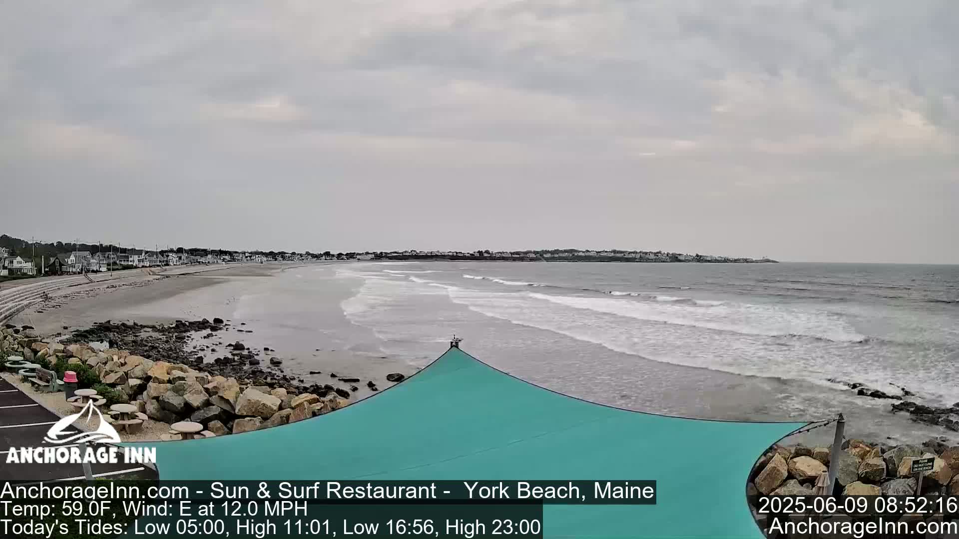 A mostly cloudy day reveals a beach with gentle waves lapping the shore, backed by a line of buildings.