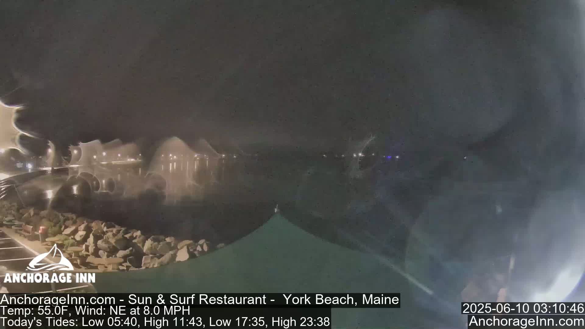 A nighttime view of a rocky shoreline and calm water under a dark, overcast sky.