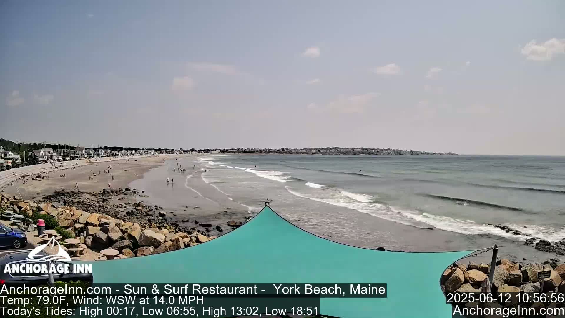 A sandy beach with small waves and scattered people is visible, under a mostly clear sky.