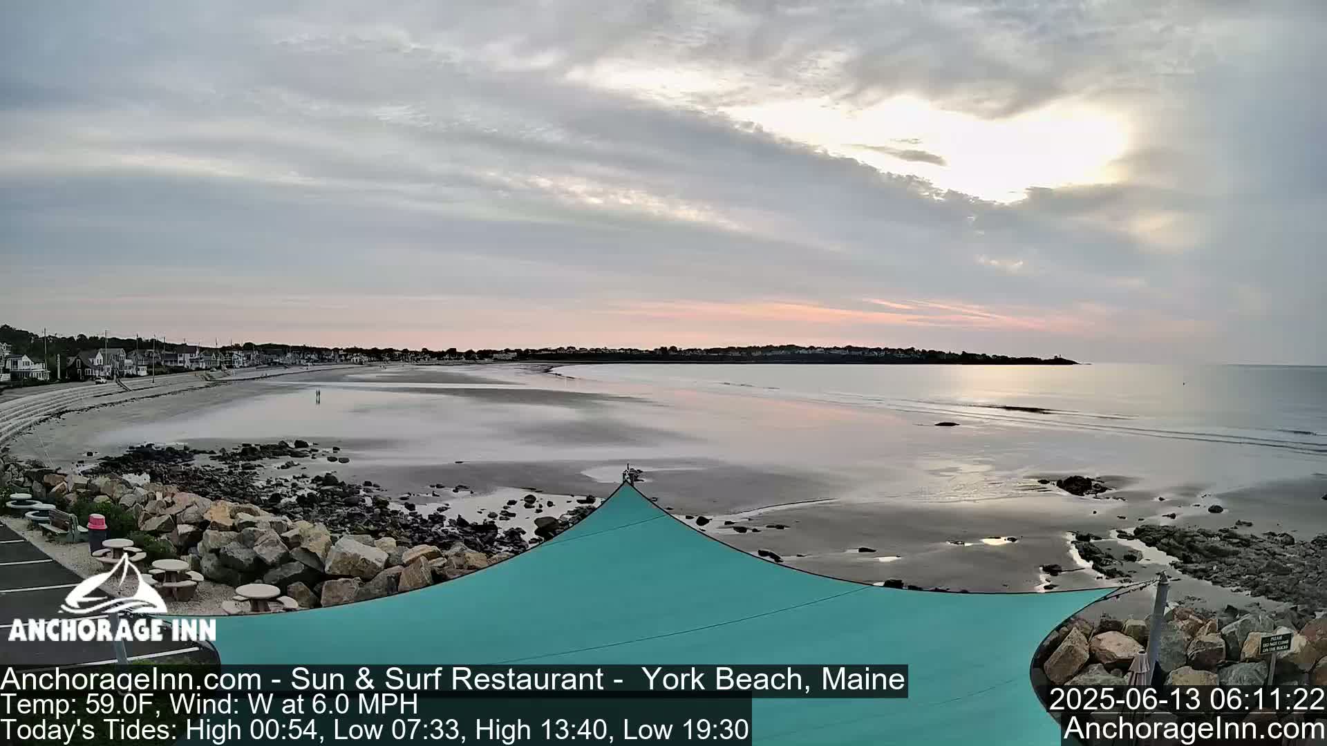 A tranquil beach scene at sunrise, showing a calm ocean reflecting the pale sky, with a sandy shore and a teal sunshade in the foreground.