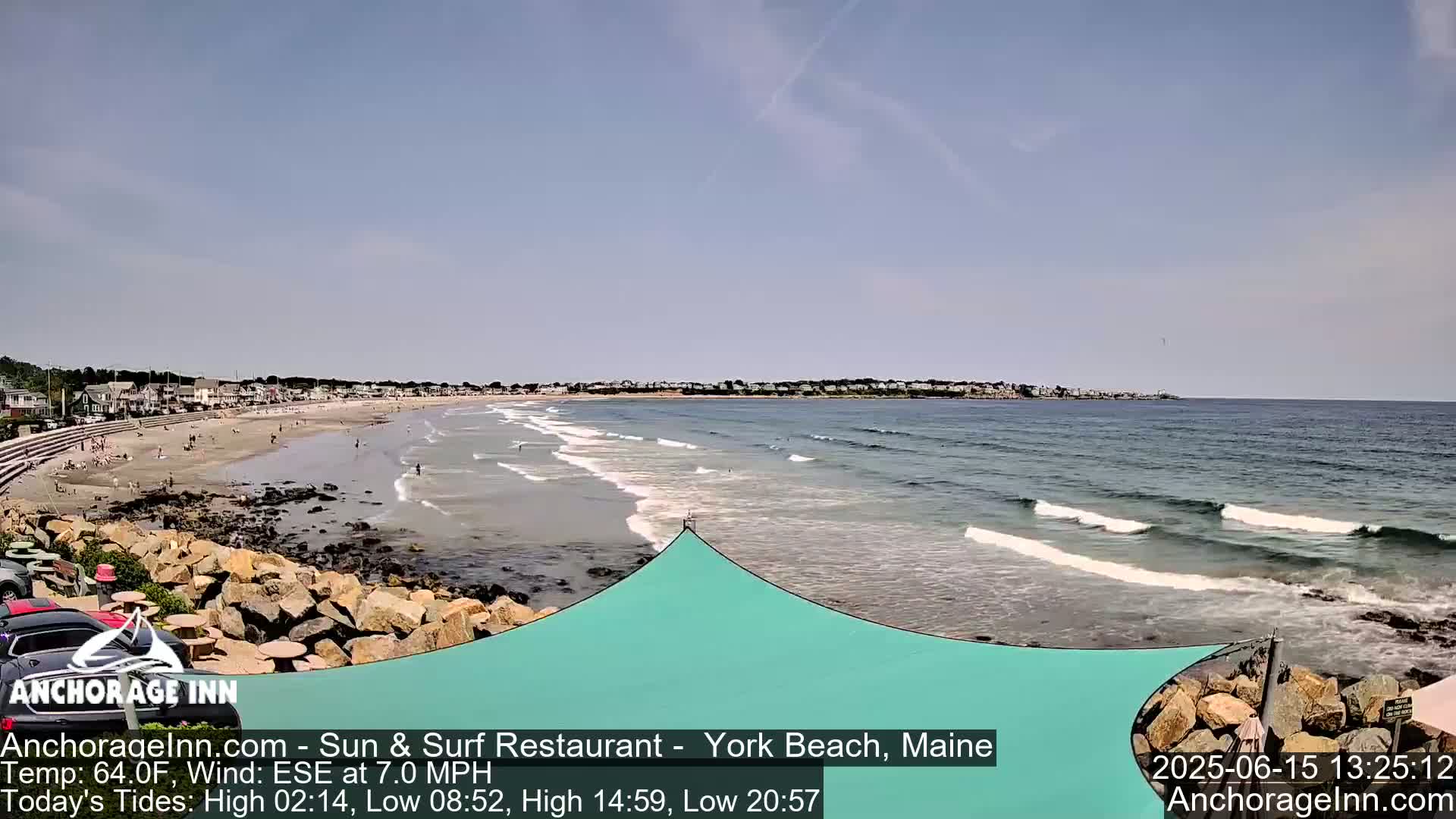 A sandy beach with small waves laps the shore under a clear sky, with a town visible in the distance.