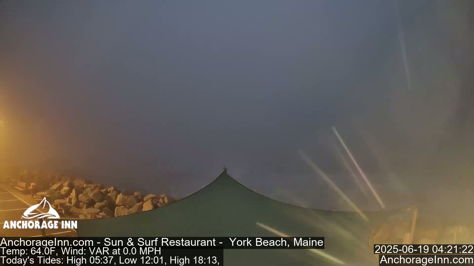 A foggy coastal scene shows a rocky shoreline and a green awninged structure under a hazy, dark sky.