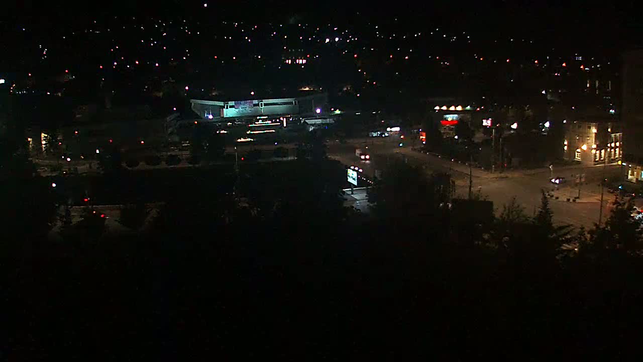 A nighttime aerial view shows a city with dimly lit buildings, streets, and sparse traffic.