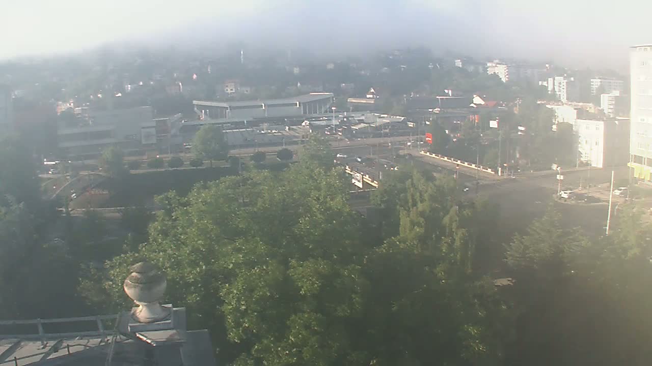 A foggy view of a city intersection with buildings, roads, and green trees, seen from an elevated perspective.