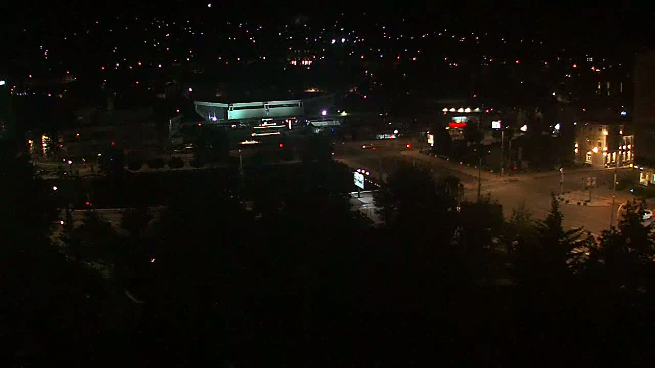 A nighttime aerial view of a city with scattered lights, a large building, and roadways.