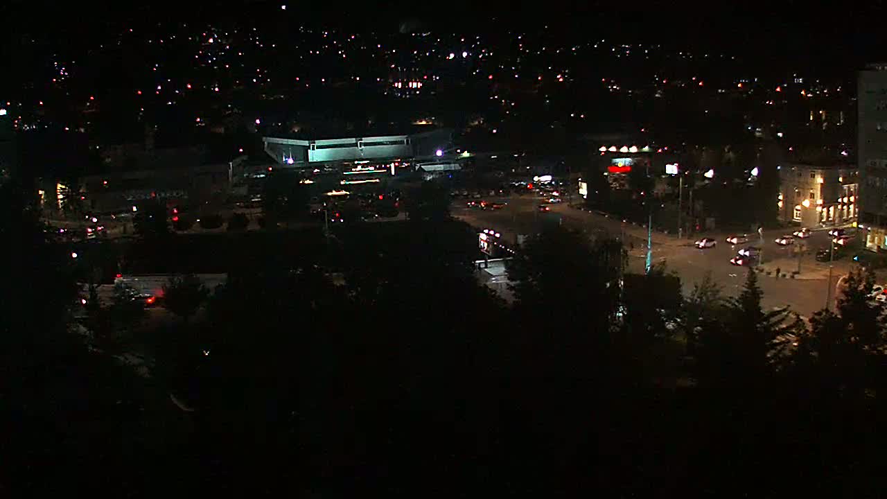 A nighttime aerial view of a city with illuminated buildings and roads, showing sparse vehicle traffic.