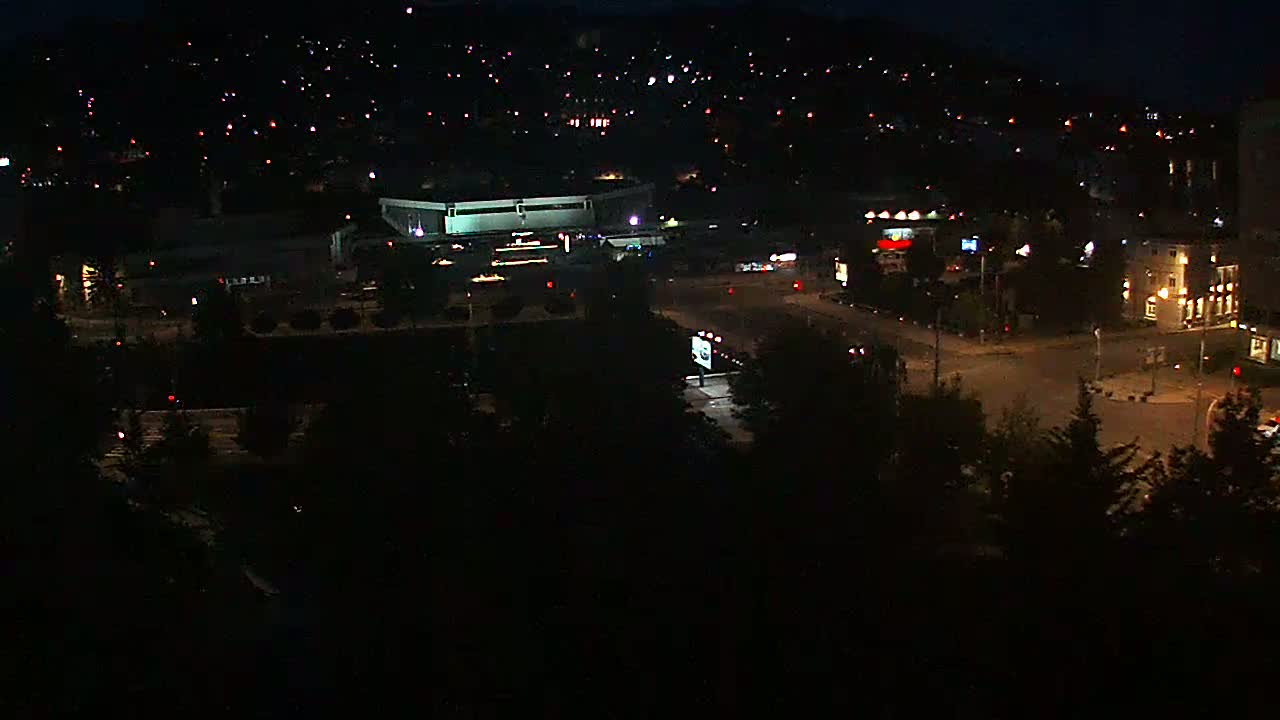 A nighttime aerial view of a city intersection with a large building and surrounding residential areas under a clear, dark sky.