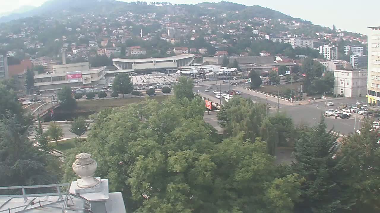A hazy view of a city nestled in a hillside, showing a large building, a bridge, roadways, and green spaces.