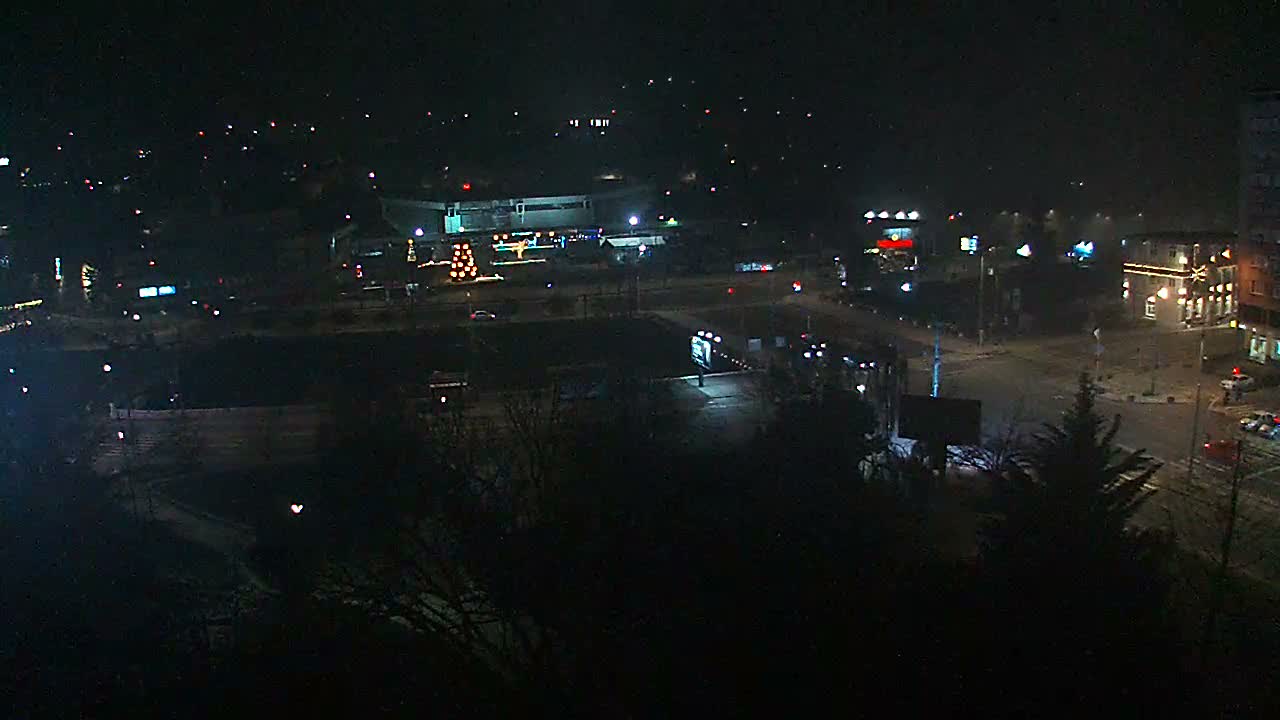 The image displays a clear, dark outdoor night scene of a city area with numerous illuminated buildings, streets with vehicle lights, and decorative lights, with the ground appearing wet but no active precipitation.