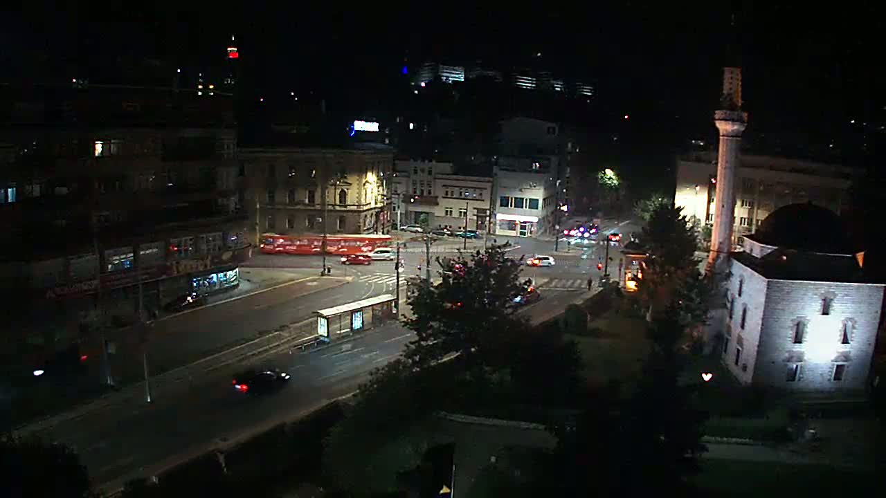 A nighttime, high-angle view of a city street intersection with several buildings, including a mosque, and cars driving on the road.