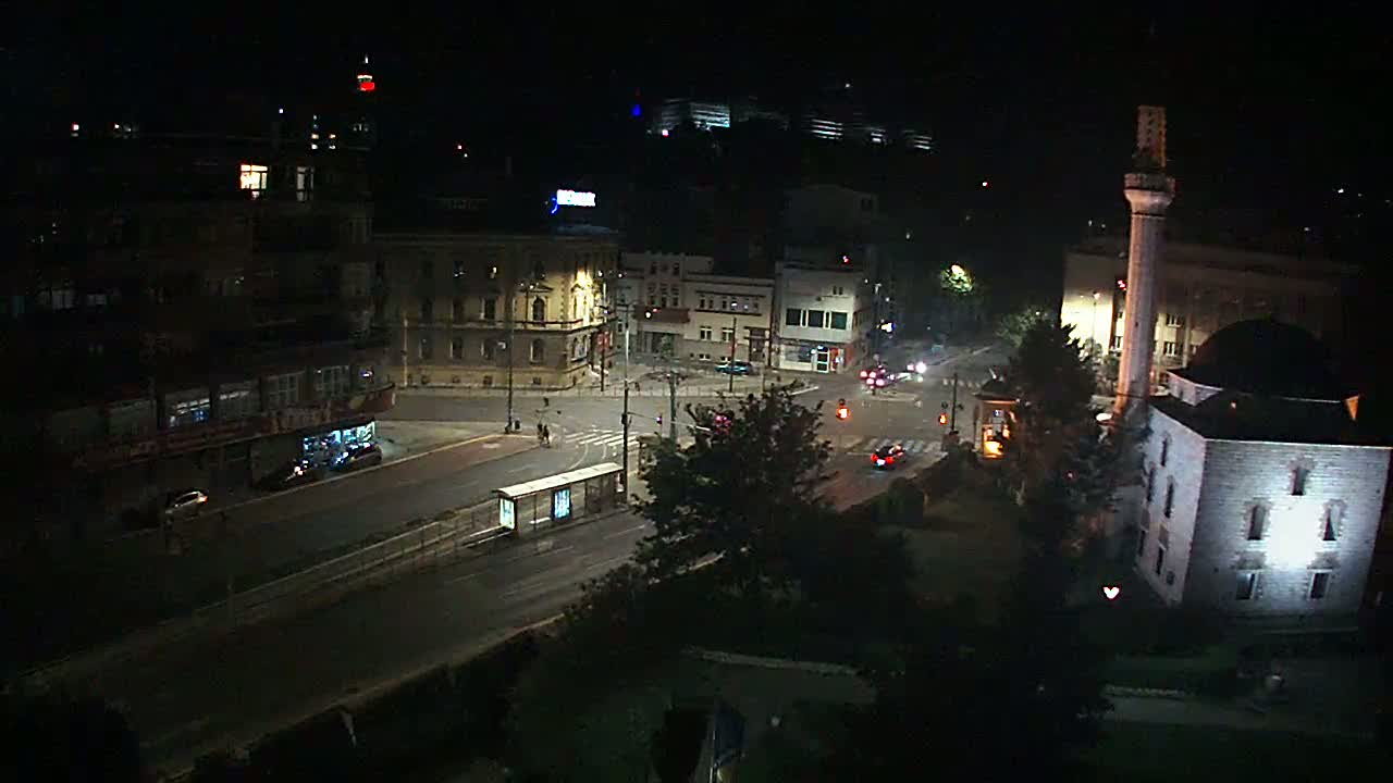 A nighttime, high-angle view of a city intersection with a mosque and several buildings, showing a few cars and minimal pedestrian activity.