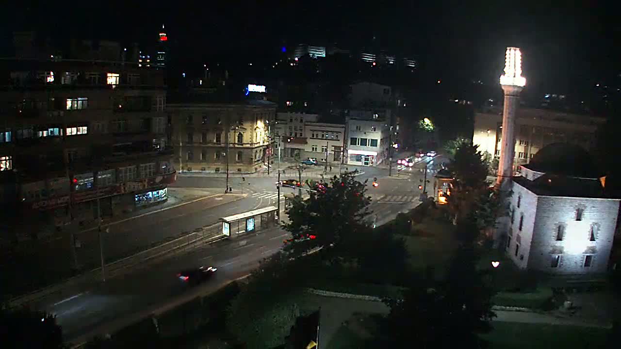 A nighttime street scene shows a city intersection with buildings, a mosque with a lit minaret, and sparsely trafficked roadways.