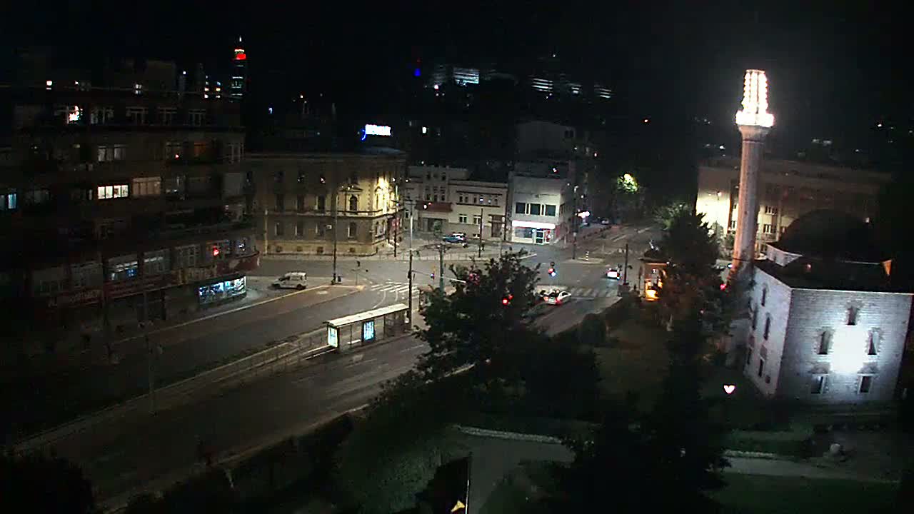 A nighttime aerial view of a city street intersection with buildings, a mosque, and sparse vehicle traffic under dark conditions.
