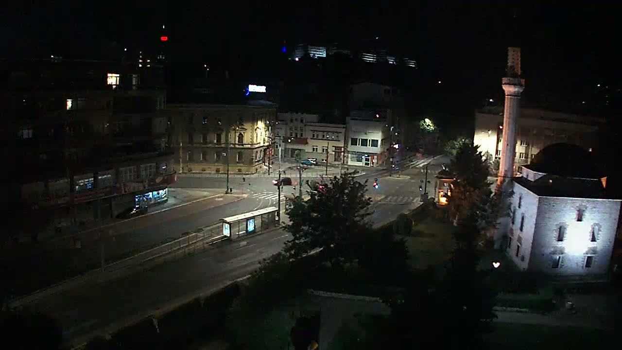A nighttime, street-level view of a city intersection with buildings, including a mosque, illuminated by streetlights.