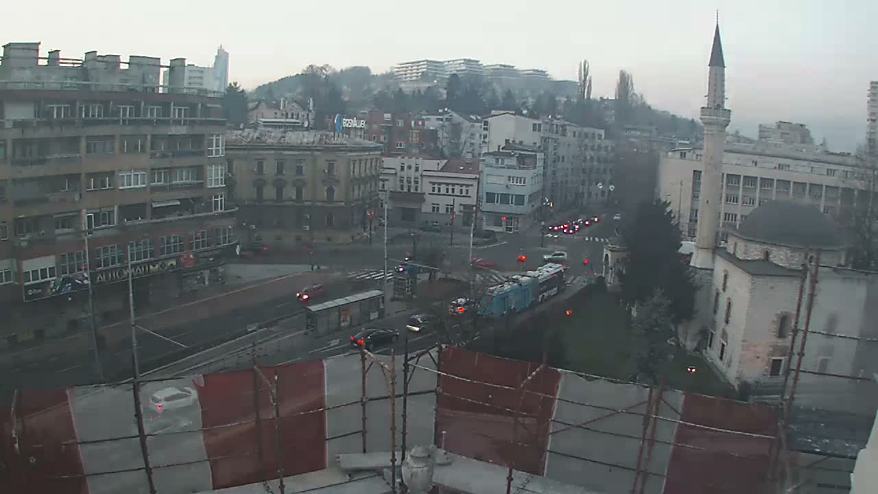 An elevated nighttime view shows a city intersection with moving cars and illuminated buildings, including a prominent mosque with its minaret, under slightly hazy conditions.