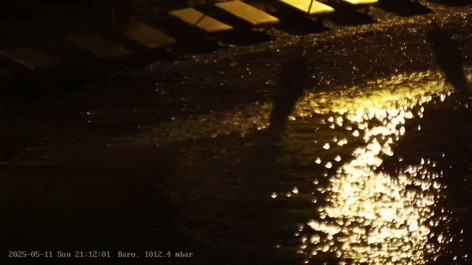 Illuminated water droplets cascade down a dark surface at night.