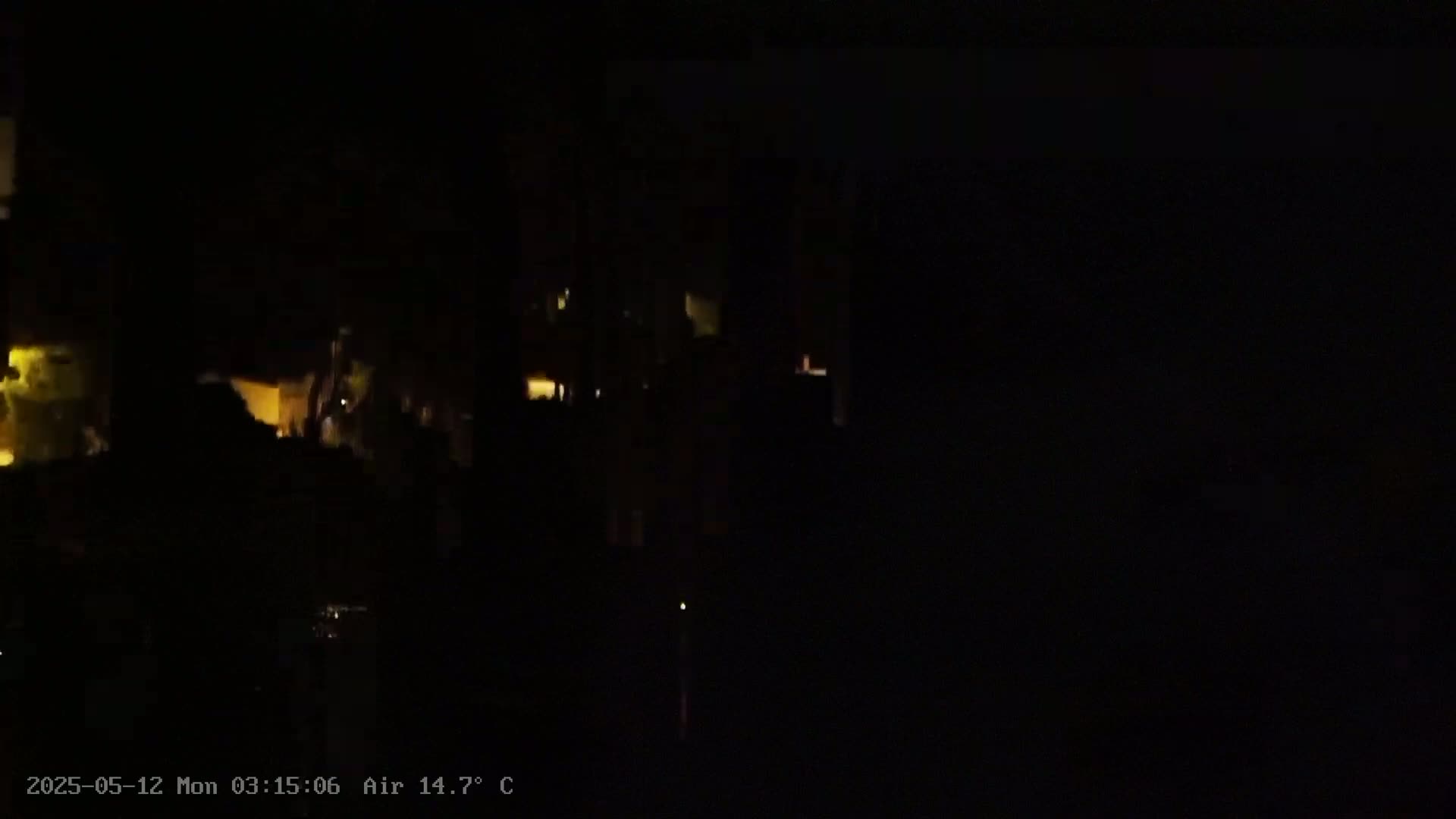 A nighttime, low-light view shows dimly lit buildings and vegetation under a dark sky with an air temperature of 14.7 degrees Celsius.
