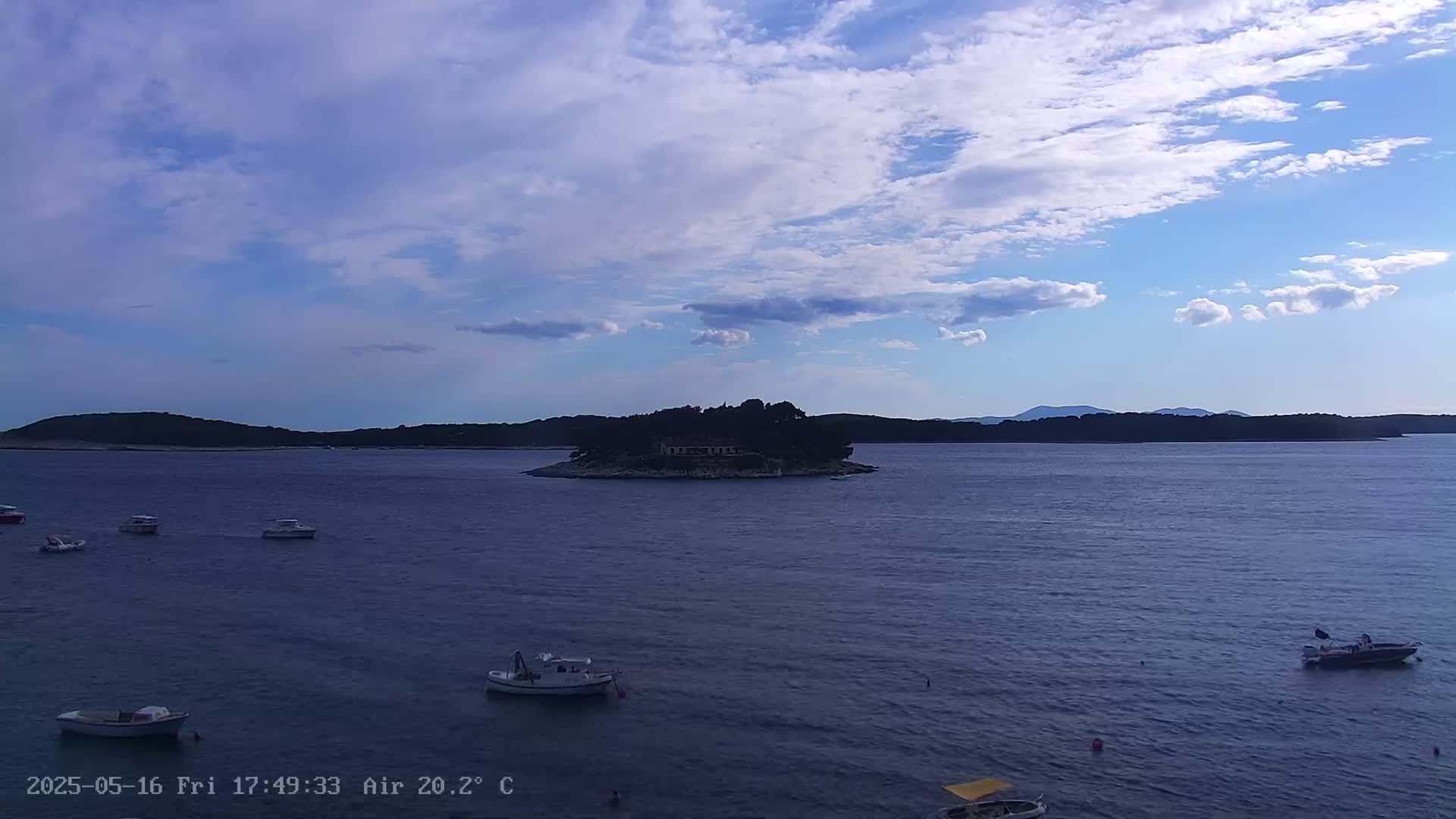 A small island with a building on it sits in a calm sea under a partly cloudy sky.