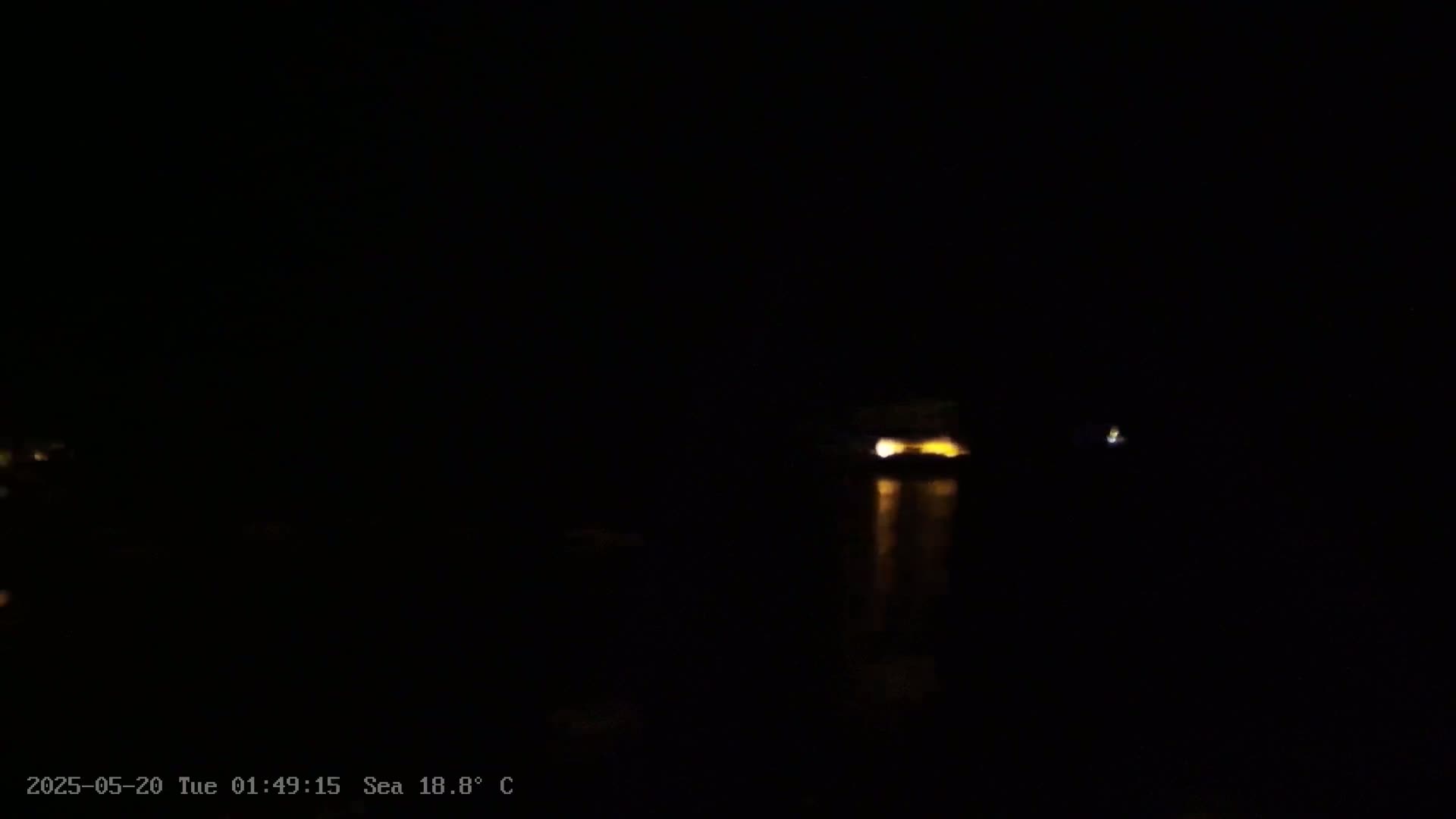 A dimly lit structure is visible across a dark body of water at night, under a clear sky.
