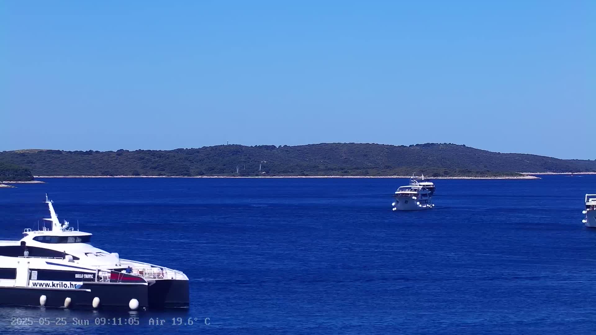 Three boats are on a deep blue sea under a clear blue sky, with a dark green, hilly island in the background.