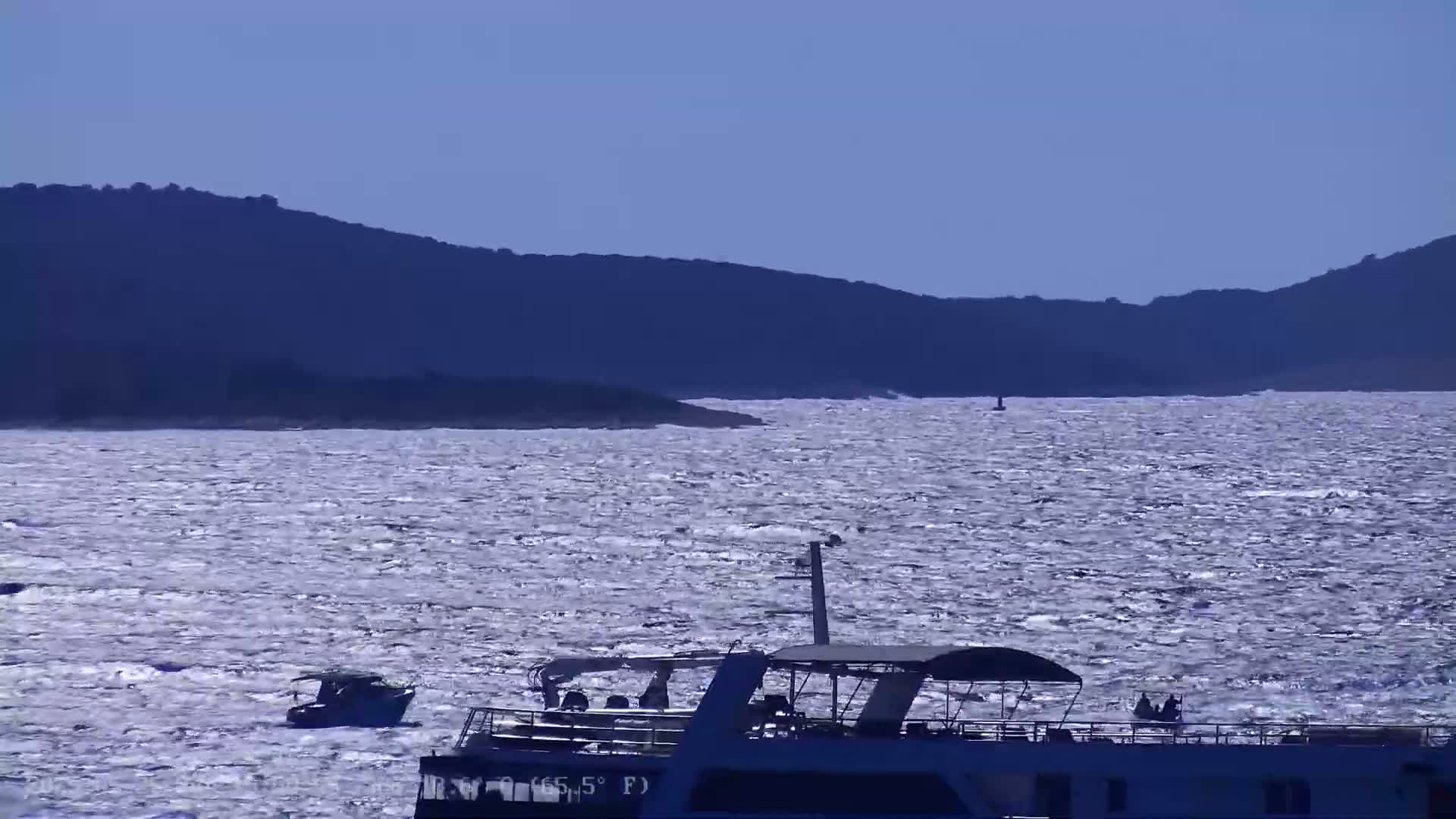 A large passenger boat and a smaller boat are on a wavy sea with dark hills in the background under a clear sky.