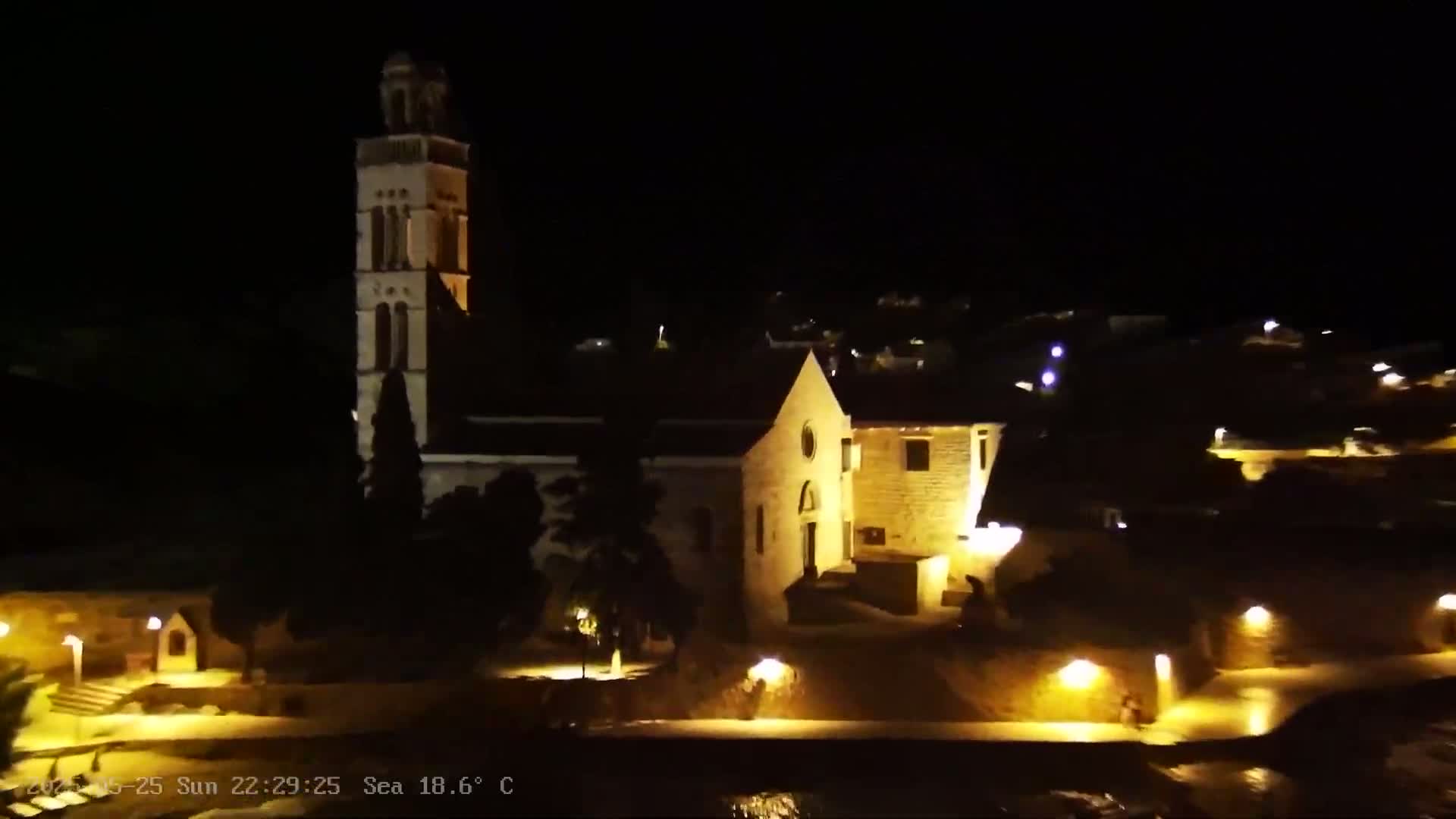 A church and surrounding buildings are illuminated at night, with the sea visible in the foreground.