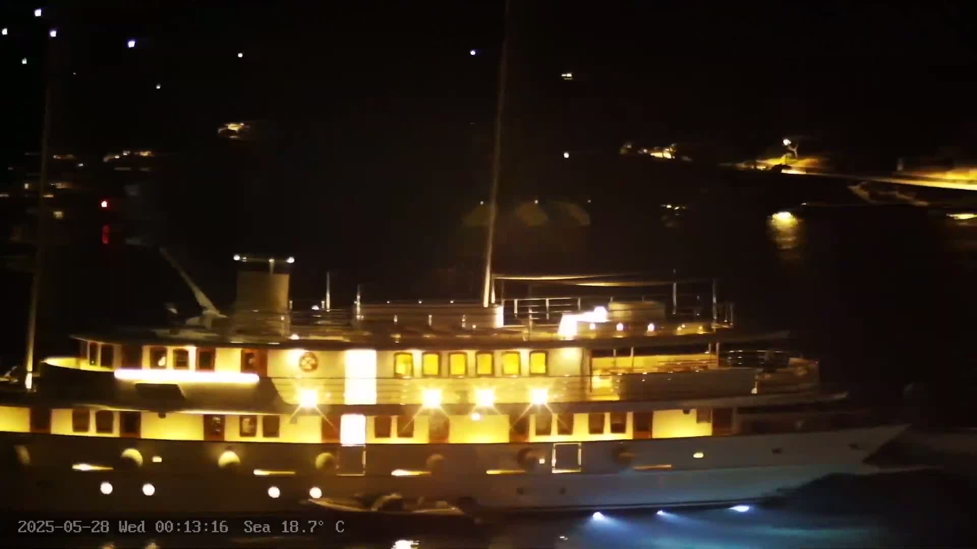 A large, brightly lit yacht is docked at night in calm water, with other boats visible in the distance.