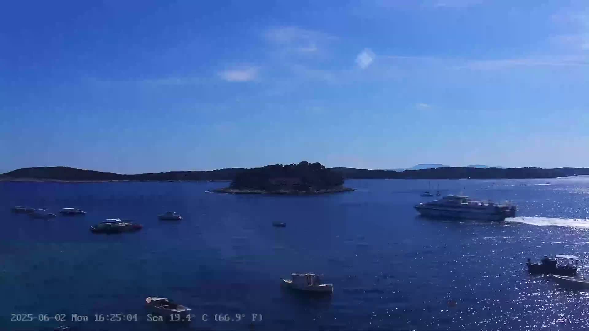 A small island is visible in a calm, blue sea under a clear blue sky, with several boats scattered across the water.