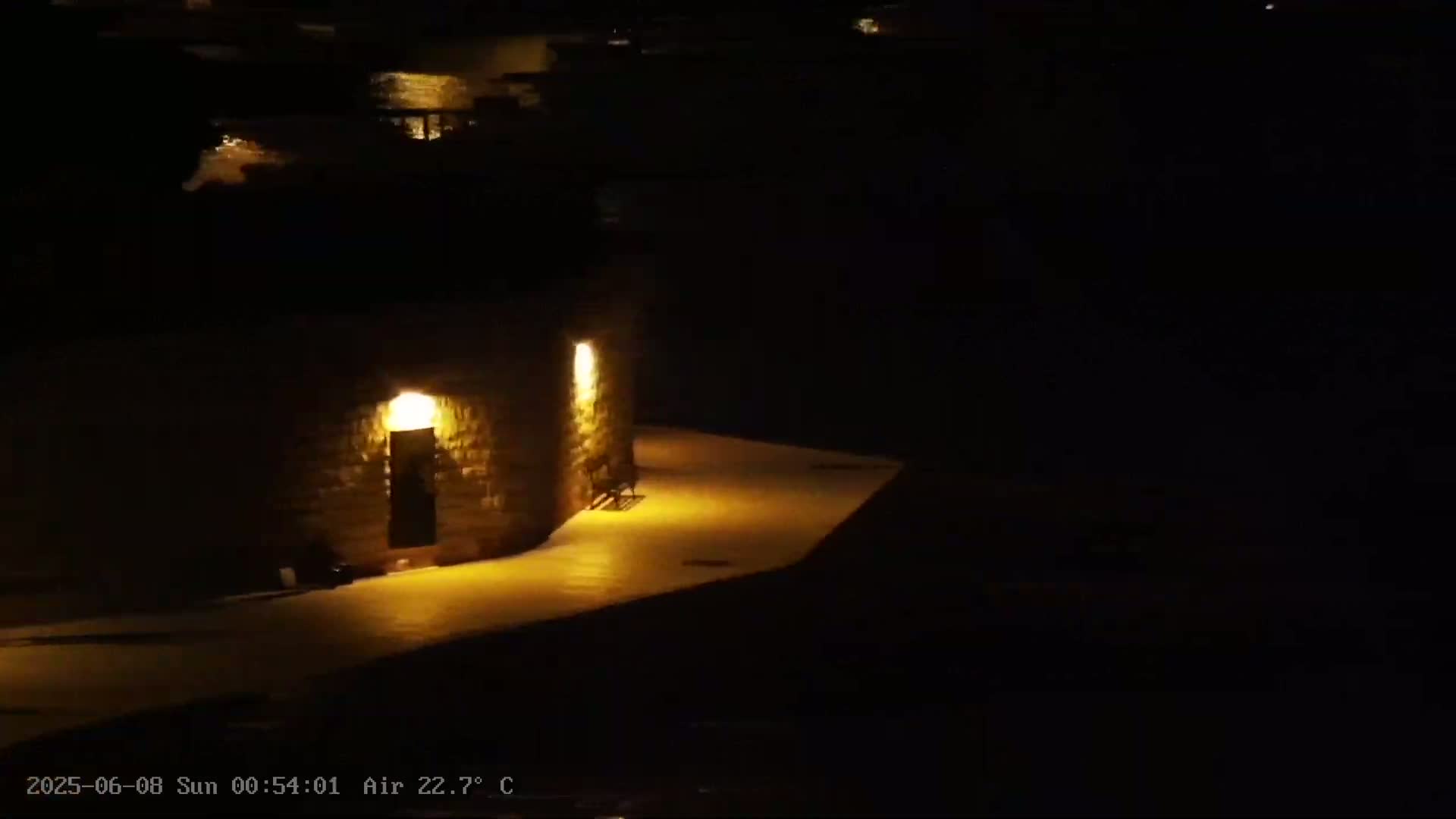 A stone structure with lit doorways is illuminated at night near a dark body of water.