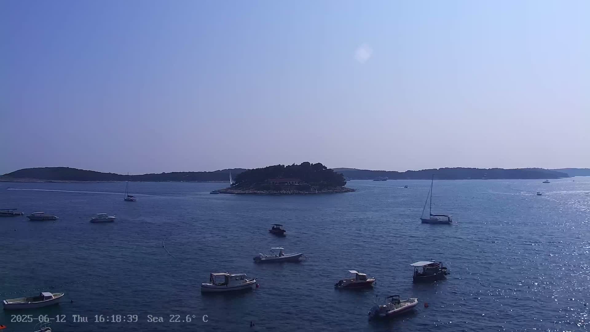 A calm, sunny day shows a small island with buildings surrounded by numerous boats in a bay.