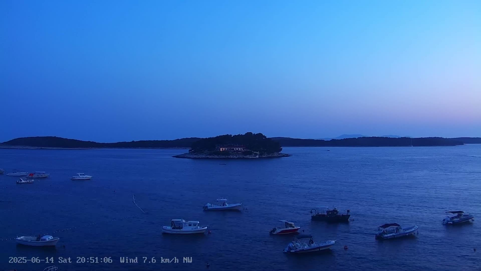 A sailboat is anchored in a calm, blue sea near a rocky outcrop on a clear, sunny day.