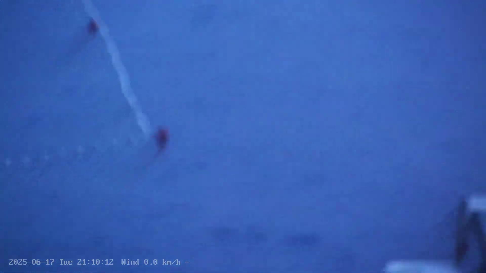Two small, indistinct red objects are visible on a large, dark blue surface under calm, windless conditions.
