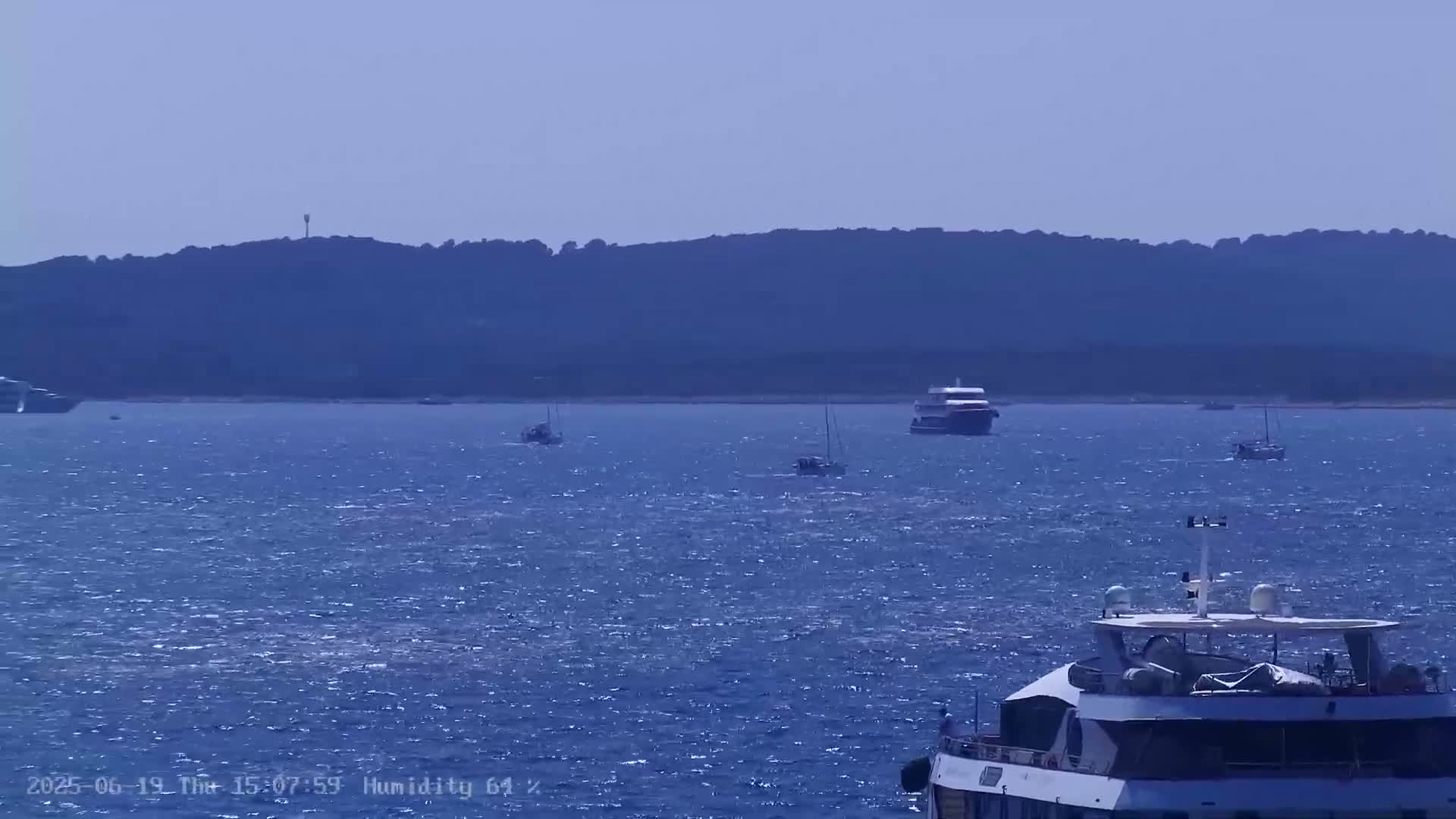 Several boats are visible on a somewhat choppy blue sea, with a dark-colored landmass in the background under a clear sky.