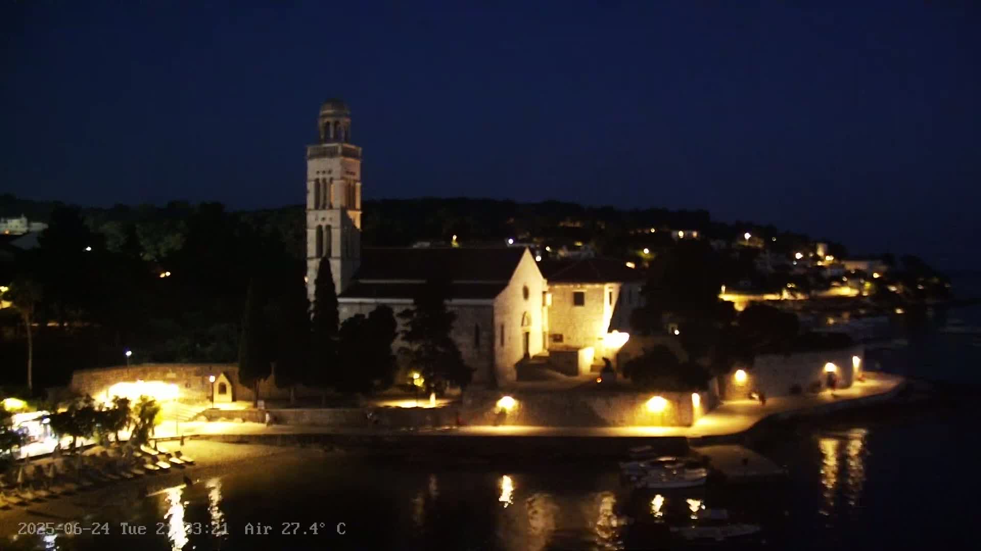 A church and surrounding buildings are illuminated at night, overlooking a calm body of water under a dark sky.