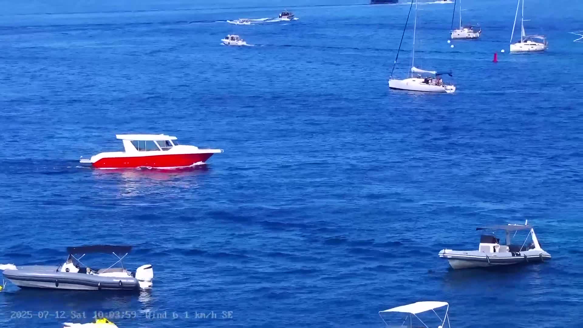 Several boats and sailboats are floating on a calm, blue ocean under a clear sky.