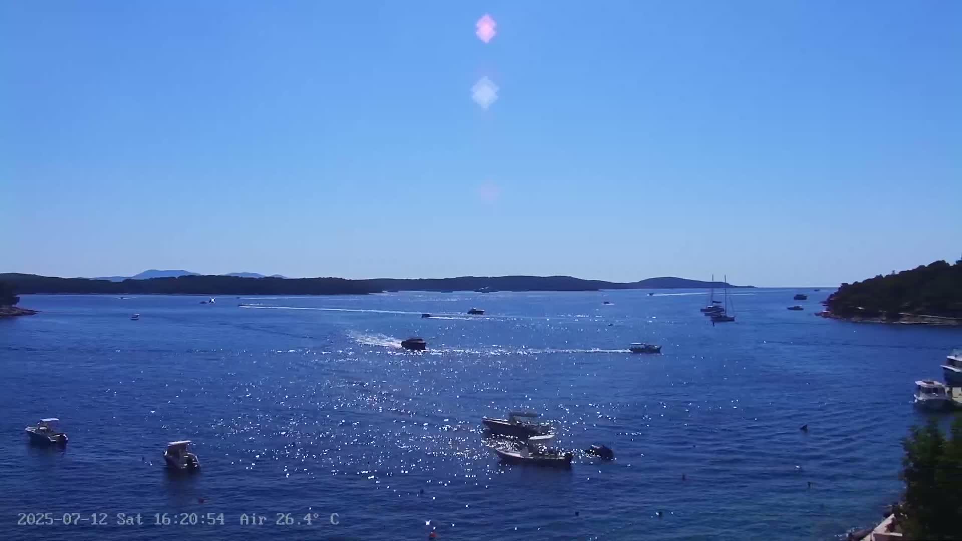 Several boats and sailboats are floating on a calm, blue ocean under a clear sky.
