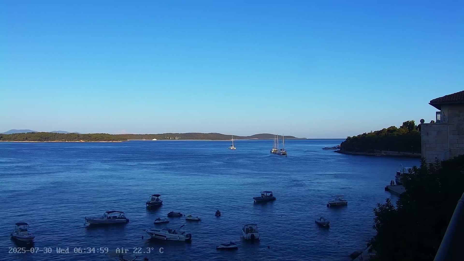 Several small motorboats are moored in calm, blue water, with a line of white buoys visible in the foreground.